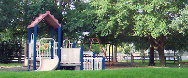 Playground toy with slides set in a park with trees and a fence.